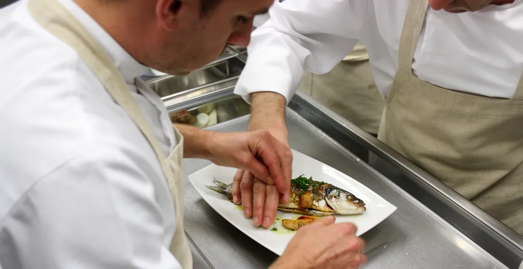 Chef dressant un plat de poisson du lac d'Annecy en cuisine professionnelle