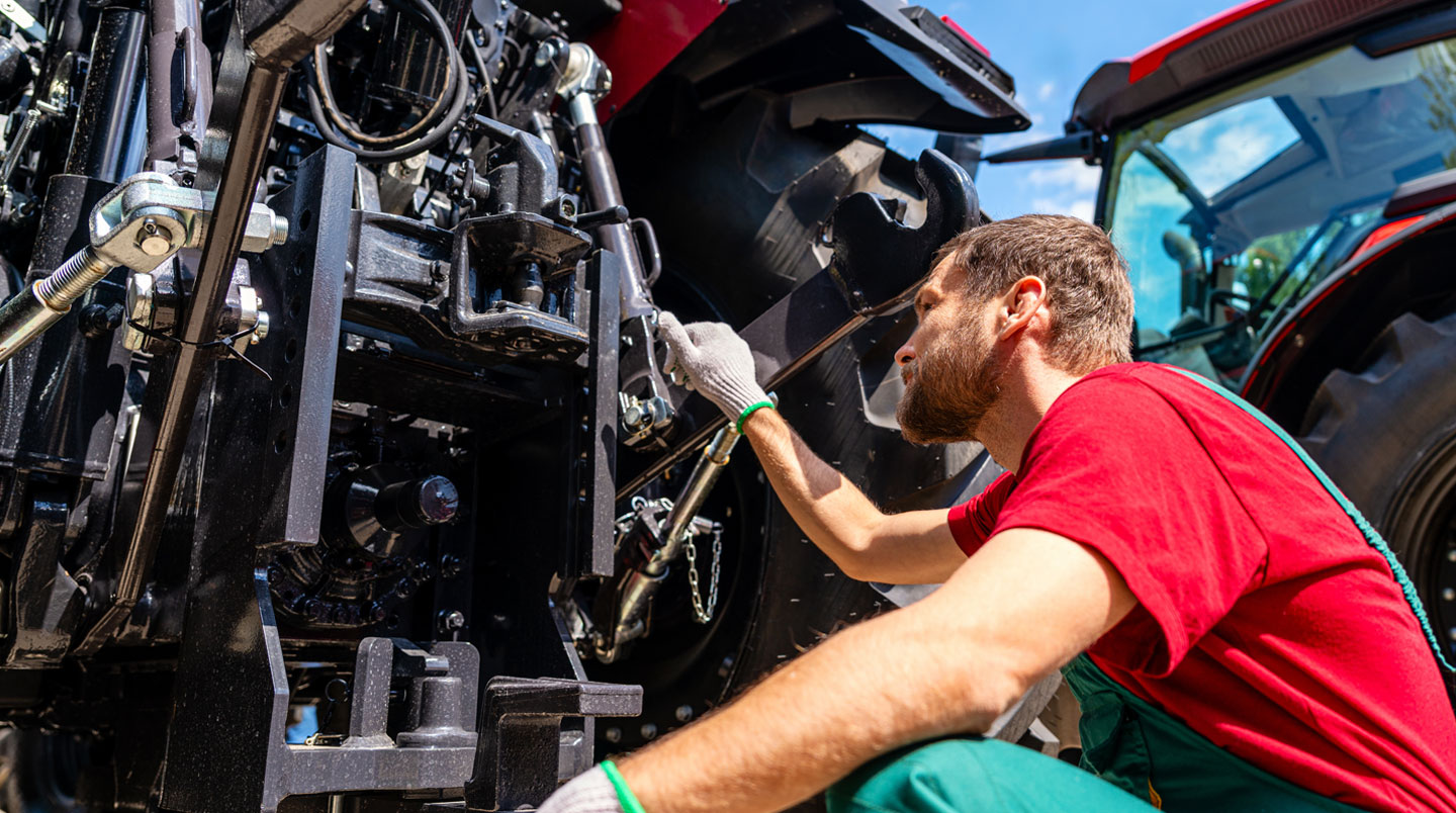 Mécanicien agricole inspectant la zone de transmission sous un tracteur dans un atelier rural