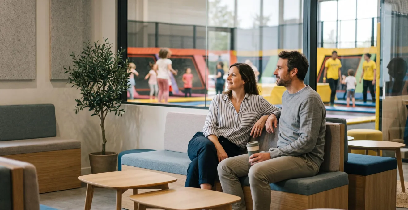 Parents détendus assis dans l'espace accompagnants climatisé d'un trampoline park tout en surveillant leurs enfants jouer au loin