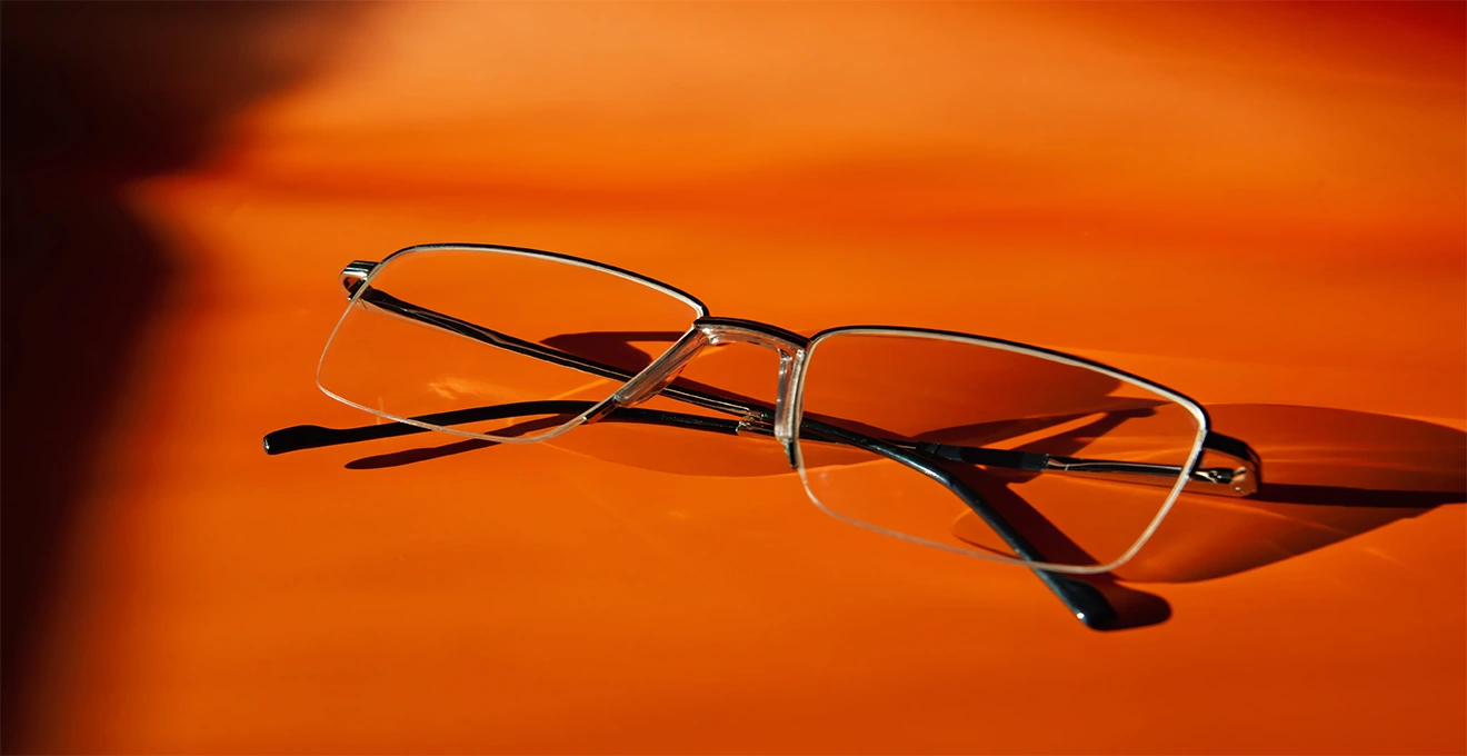 Un homme essaie des lunettes demi-cerclées devant un miroir accompagné d'un opticien.
